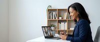Professional African American businesswoman in navy blazer participating in video conference call on laptop at modern home office workspace.