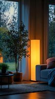 Cozy evening living room corner with tall glowing floor lamp casting warm light, houseplant by window, and comfortable sofa against twilight outdoor view.