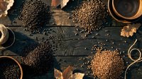 Assorted organic legumes and grains displayed on rustic wooden background with autumn leaves and ceramic bowls for healthy cooking and nutrition.