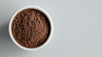 Ground coffee powder in white ceramic bowl on gray background, top view. Fresh roasted arabica coffee with rich dark brown color and fine texture.