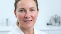 Middle-aged Caucasian female healthcare professional smiling warmly in modern medical office setting wearing white coat for medical and wellness concepts.