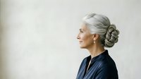 Mature woman with gray hair styled in elegant updo, wearing dark navy blouse, profile view against neutral background. Suitable for healthcare, wellness, aging gracefully, and professional portraits.