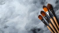 Professional artist paintbrushes with wooden handles and dark bristles arranged on textured gray concrete background for creative projects.