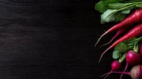 Fresh red radishes with green leaves on dark wooden background, top view with copy space for text. Natural organic vegetables for healthy eating.