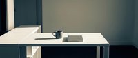 Minimalist workspace with white desk, black mug, and notebook against teal wall, suitable for office, business, and productivity concepts.