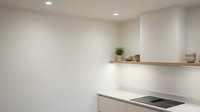 Modern minimalist kitchen interior with white walls, wooden floating shelf, ceramic bowls and small potted plant creating clean contemporary cooking space.
