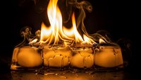 Ice cubes melting with dramatic flames rising from surface creating striking contrast between fire and ice elements on dark background.
