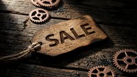 Wooden sale tag with engraved text on rustic dark wood surface surrounded by copper gears, evoking a vintage industrial retail concept.