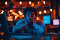 Young African American man looking stressed and overwhelmed in dimly lit bar or restaurant with warm bokeh lights creating moody atmosphere for mental health concepts.