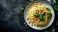 Spaghetti pasta with chickpeas and fresh basil leaves served on gray ceramic plate against dark background. Mediterranean cuisine for healthy eating.