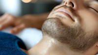 Close up portrait of relaxed young caucasian man with trimmed beard lying with closed eyes on massage table at wellness spa center during treatment session.
