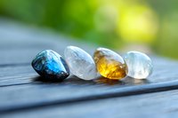 Healing crystals and gemstones lined up on wooden surface in sunlight - labradorite, clear quartz, amber, and moonstone for meditation and spiritual practices.