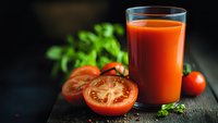Fresh tomato juice in glass with sliced tomatoes and herbs on dark wooden table for healthy breakfast and organic nutrition lifestyle.