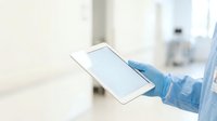 Healthcare professional wearing blue protective gloves holding blank mobile device screen in sterile medical environment for telemedicine consultation.