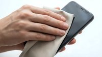 Male hand with medium skin tone holding smartphone while wiping screen with microfiber cloth for cleaning and maintenance purposes.
