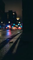Blurred city street at night with colorful bokeh lights reflecting on wet asphalt pavement creating atmospheric urban mood for backgrounds and design projects.