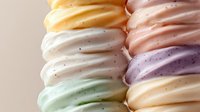 Colorful soft serve ice cream swirls in pastel shades of yellow, pink, white, purple, mint green, and peach stacked together against neutral background.