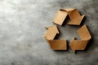 Recycling symbol made from brown cardboard arrows on textured gray concrete background, representing sustainability and eco-friendly packaging solutions.