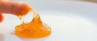 Stretchy orange slime being pulled and extended between fingers against white background, perfect for toy product marketing and educational content.