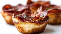 Crispy bacon wrapped around golden baked muffins creating savory breakfast treats with caramelized edges on white background isolated for culinary designs.