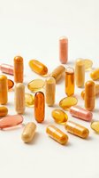 Assorted vitamin supplements and capsules in orange and yellow tones scattered on neutral background for health and wellness concepts.