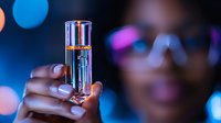 Young African American woman holding elegant perfume bottle against blurred bokeh lights background, luxury fragrance and beauty concept.