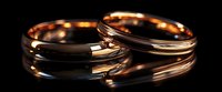 Elegant rose gold wedding bands with reflective surface on dark background, showcasing fine jewelry craftsmanship and romantic symbolism. For wedding and engagement themes.