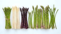 Assorted fresh asparagus bundles including green, white, and purple varieties arranged in rows on white background for culinary and food styling projects.