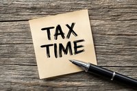 Tax time reminder written on yellow sticky note with fountain pen on rustic wooden background, concept for financial planning and tax season.