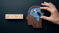 Person with hand holding glowing brain gear mechanism inside wooden head silhouette next to mind text blocks on dark background for psychology and mental health concepts.