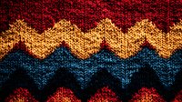 Colorful zigzag knitted pattern in red, yellow and navy blue wool creates retro chevron design. Traditional winter sweater texture closeup shows detailed yarn stitches.