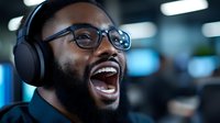 Young African American professional man wearing headphones and glasses laughing joyfully in modern office environment with bokeh lights in background.