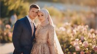 Young Muslim couple in formal attire embracing outdoors during golden hour, bride wearing hijab and groom in navy suit, romantic wedding portrait.