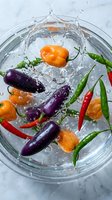 Colorful mixed hot peppers splashing in a glass bowl of water on marble surface, showcasing vibrant purple, orange, red and green chili varieties.