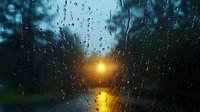 Raindrops on window glass during sunset create atmospheric mood with blurred street lights and bokeh effect in background, natural water droplets pattern on dark surface.