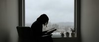 Silhouette of focused woman working on laptop by window on cloudy day. Remote work, home office, productivity and concentration concept for business content.