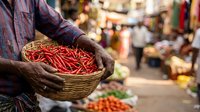 Close-up of vendor's hands holding woven basket filled with fresh red chili peppers at outdoor market. Street food and spice trading concept.