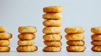 Stacked golden onion rings arranged in neat towers on white background, crispy breaded coating with deep-fried texture creates appetizing fast food composition.