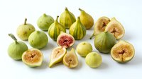 Fresh green figs whole and sliced showing pink flesh interior on white background. Organic Mediterranean fruit harvest for healthy eating and cooking.