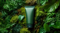Green cosmetic tube on natural moss and tropical leaves background. Organic skincare product packaging mockup surrounded by lush forest vegetation.