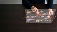 Business professional analyzing financial data on tablet with holographic interface displaying charts, graphs and analytics for investment strategy planning.