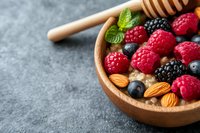 Fresh berries, almonds and honey dipper in wooden bowl on dark concrete background. Healthy breakfast ingredients with raspberries, blackberries and blueberries.