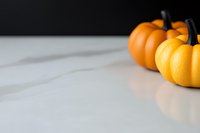 Orange decorative pumpkins on white marble surface with soft shadows and copy space. Minimalist autumn seasonal composition for holiday designs.