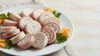 Sliced pork roulade with herb stuffing arranged on white plate with fresh parsley and orange garnish for culinary and food styling use.