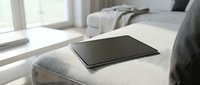 Tablet with blank black screen resting on a light gray sofa in a bright modern living room, perfect for mockup and lifestyle concepts.