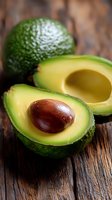Fresh ripe avocado cut in half with pit visible and whole avocado on rustic wooden background. Healthy food ingredient for cooking.