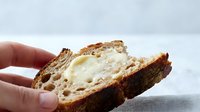 Slice of artisan sourdough bread with butter spread held in hand, showcasing texture and crumb structure for food and bakery content.