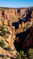 Dramatic red sandstone canyon with towering cliffs and rock formations under clear blue sky showcasing natural desert landscape geology.