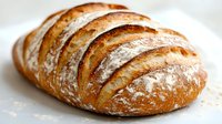 Freshly baked artisan sourdough bread with golden crust and flour dusting, showcasing distinctive scoring pattern on white background.
