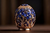 Ornate golden egg decorated with intricate blue floral patterns and filigree metalwork against dark background, luxury collectible art piece for elegant decor.
